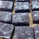 Chocolate concrete cake sliced into 12 pieces, sitting on baking paper.