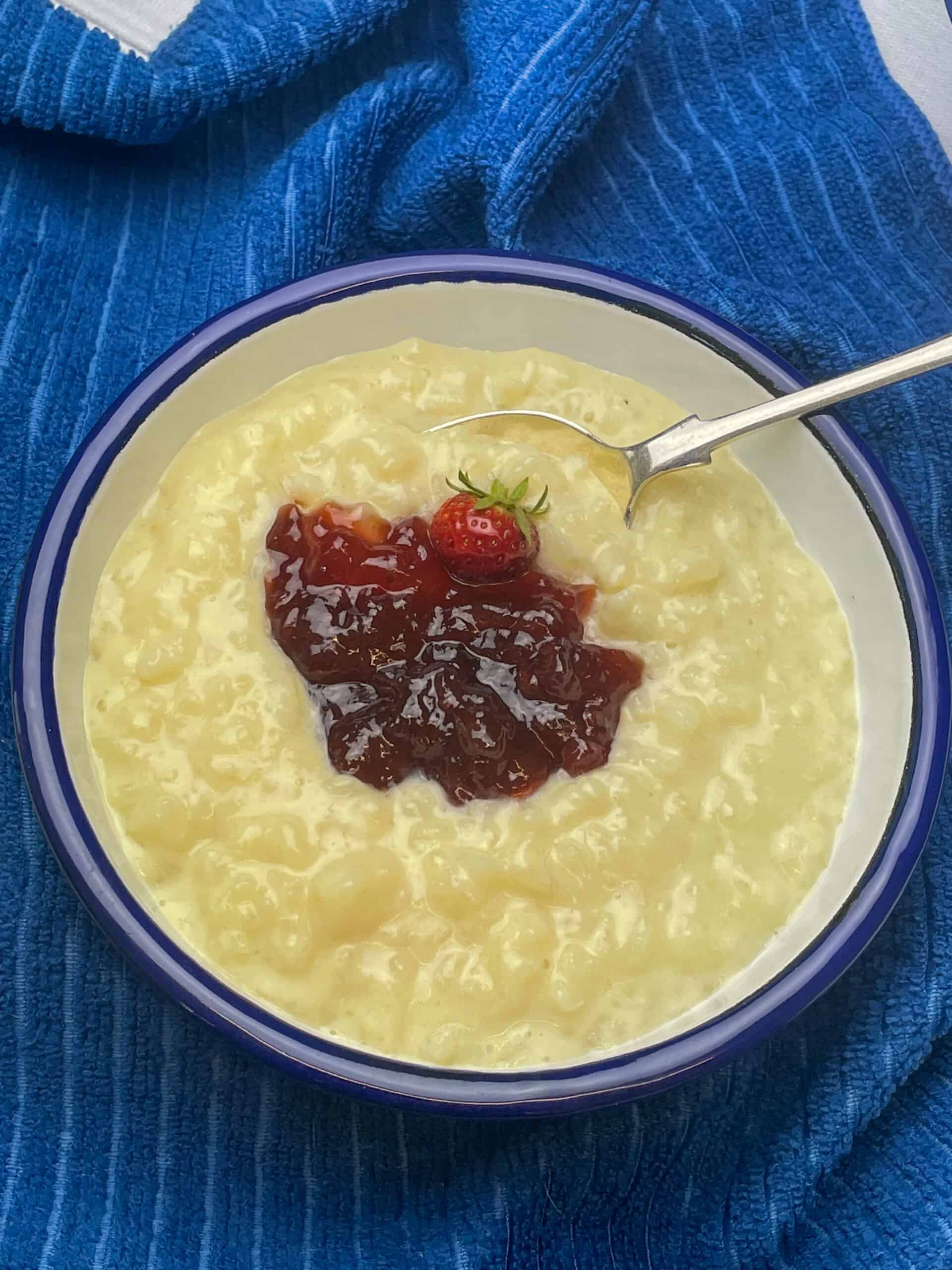 rice pudding in white bowl with blue rim and silver spoon in the pudding, blue background.