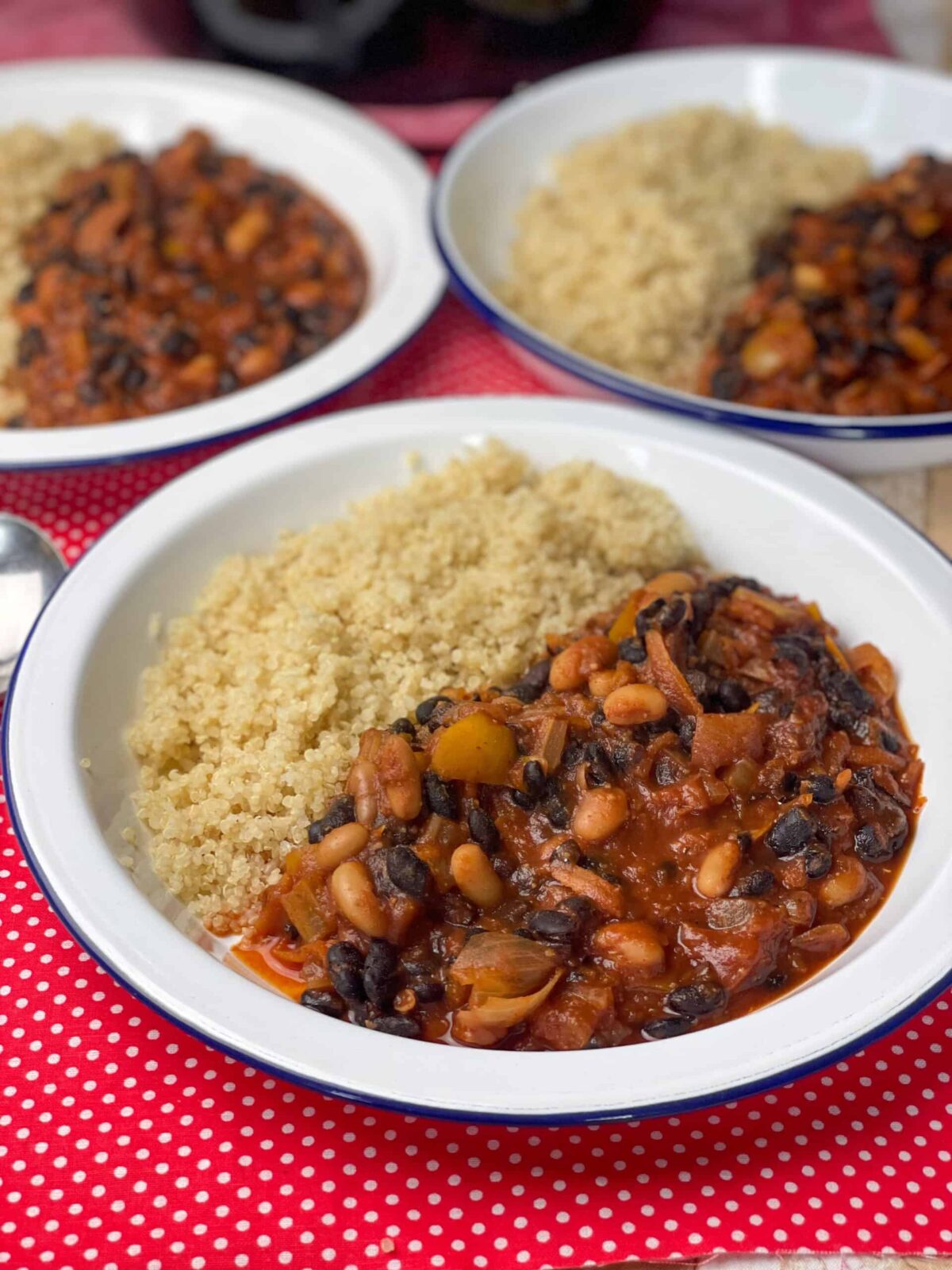 Three bowls of chilli sin carne with quinoa sitting on red check tea towel.