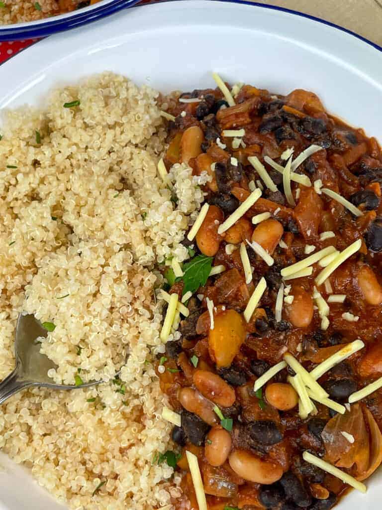 Quinoa served with chilli, with grated vegan cheese and chopped parsley.