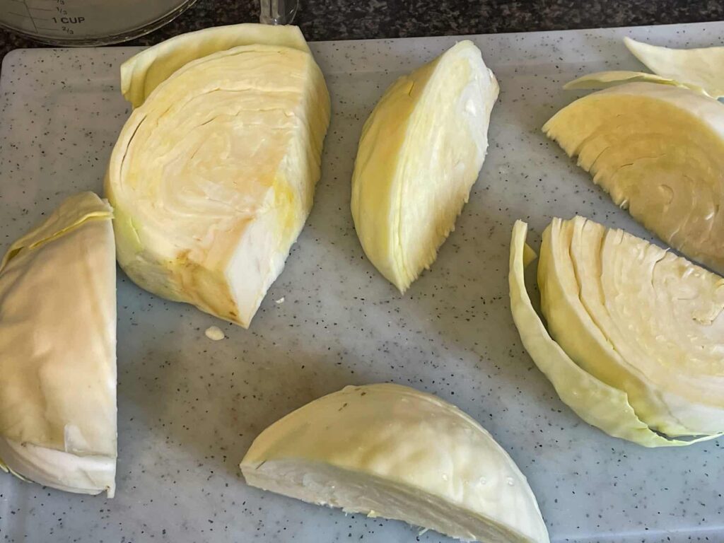 White cabbage sliced into large wedges on chopping board.