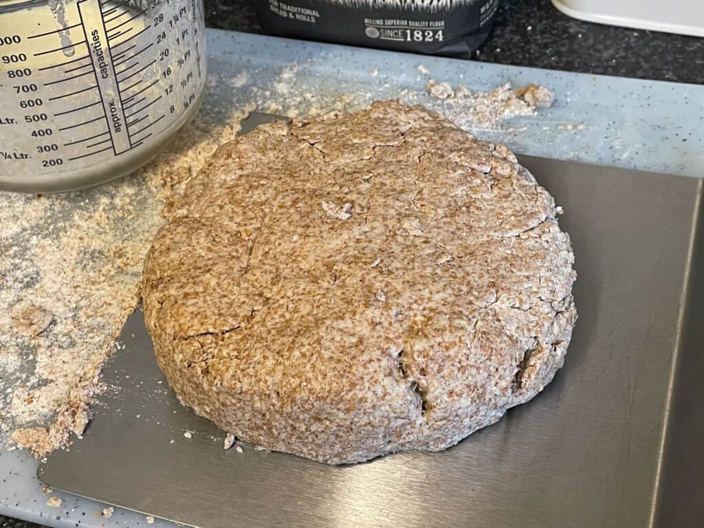 Soda bread dough sitting on metal tray, milk jug to side, sprinkle of flour on board to side.