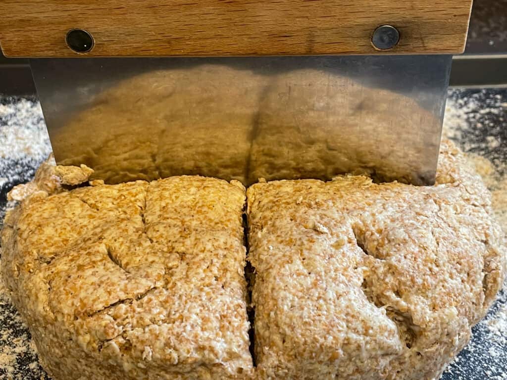 Soda bread with cross sliced across surface on work surface.