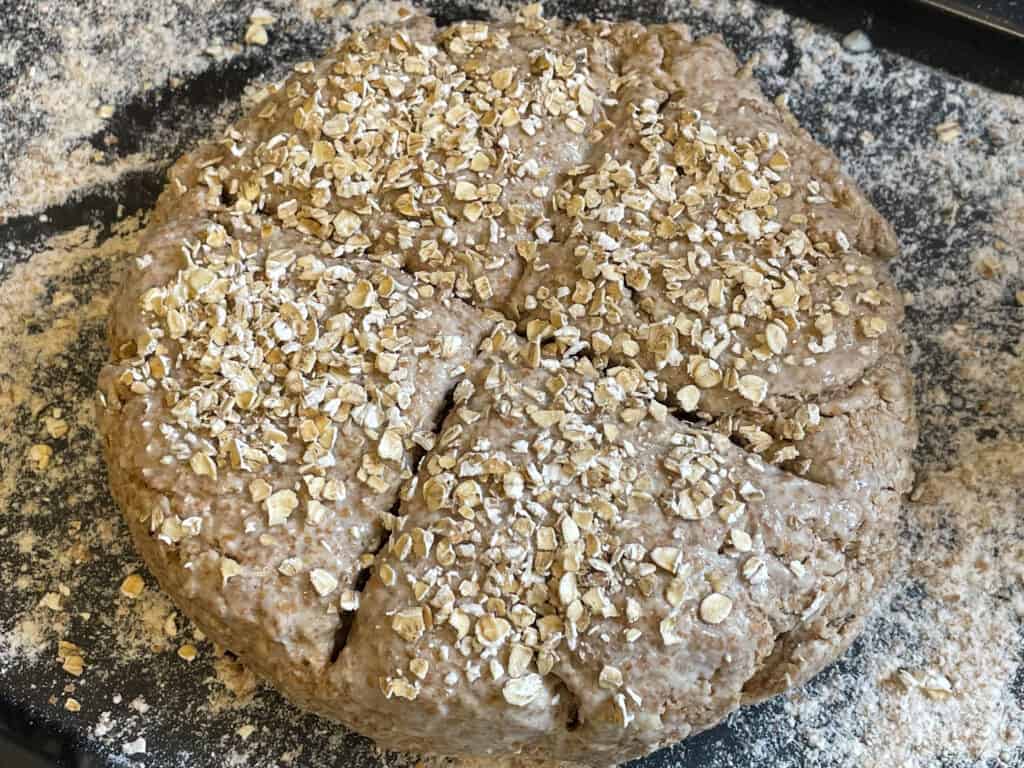 Rolled oats sprinkled over the soda bread dough, with a deep cross marked on the surface.