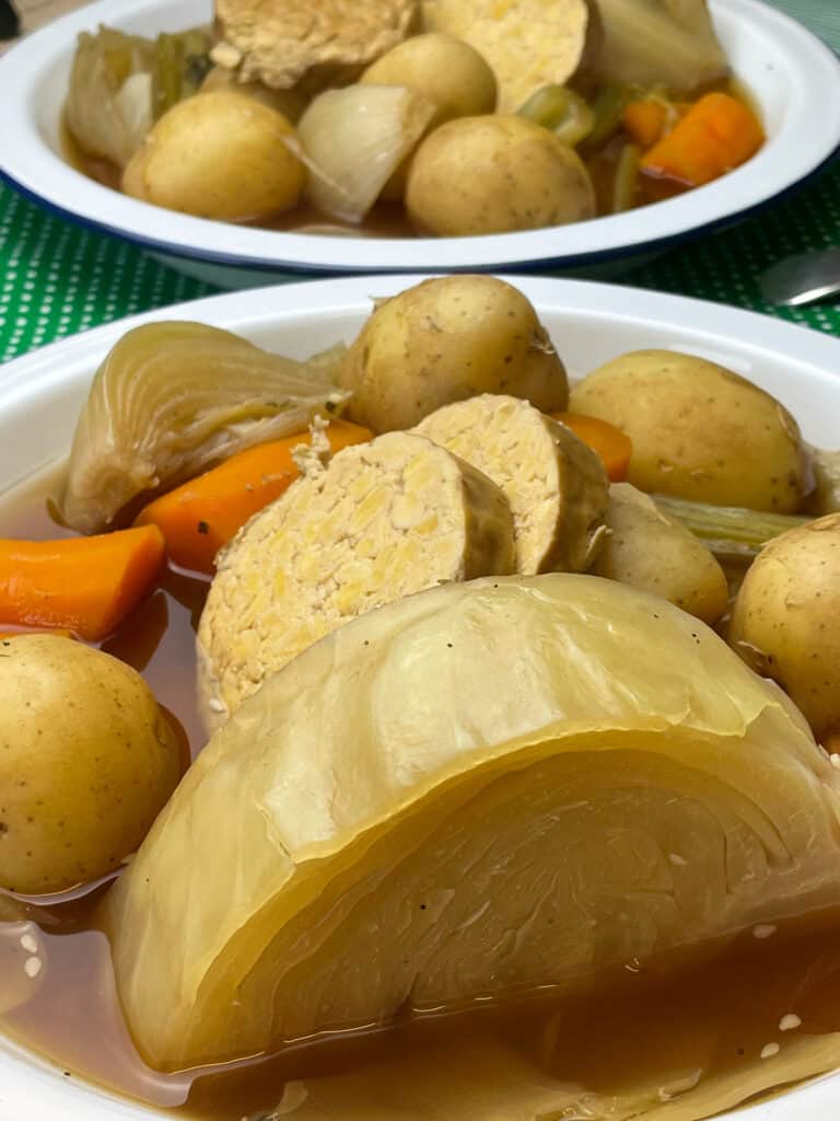 Close up of bowl of stew with large cabbage wedge to front, second bowl of stew in background.