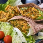 stuffed pitta breads with scrambled chickpeas and lettuce, single romaine leaf with scramble, cherry tomatoes at side of large blue plate, straw mat underneath and small blue cup to side Pinterest pin image.