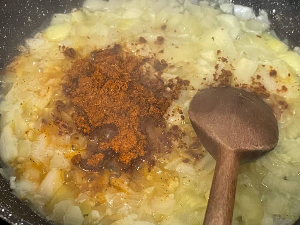 BBQ spice mix added to cooked onions, with wooden spoon.