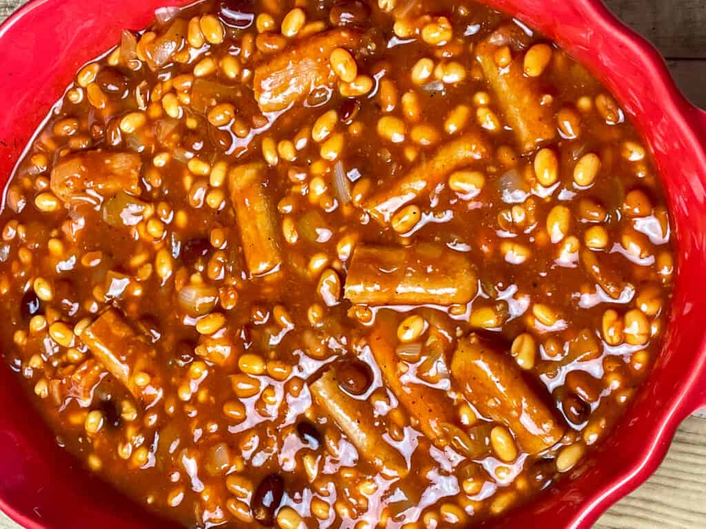 Meat-free cooked sausages added to baked bean mix in red oval casserole dish.