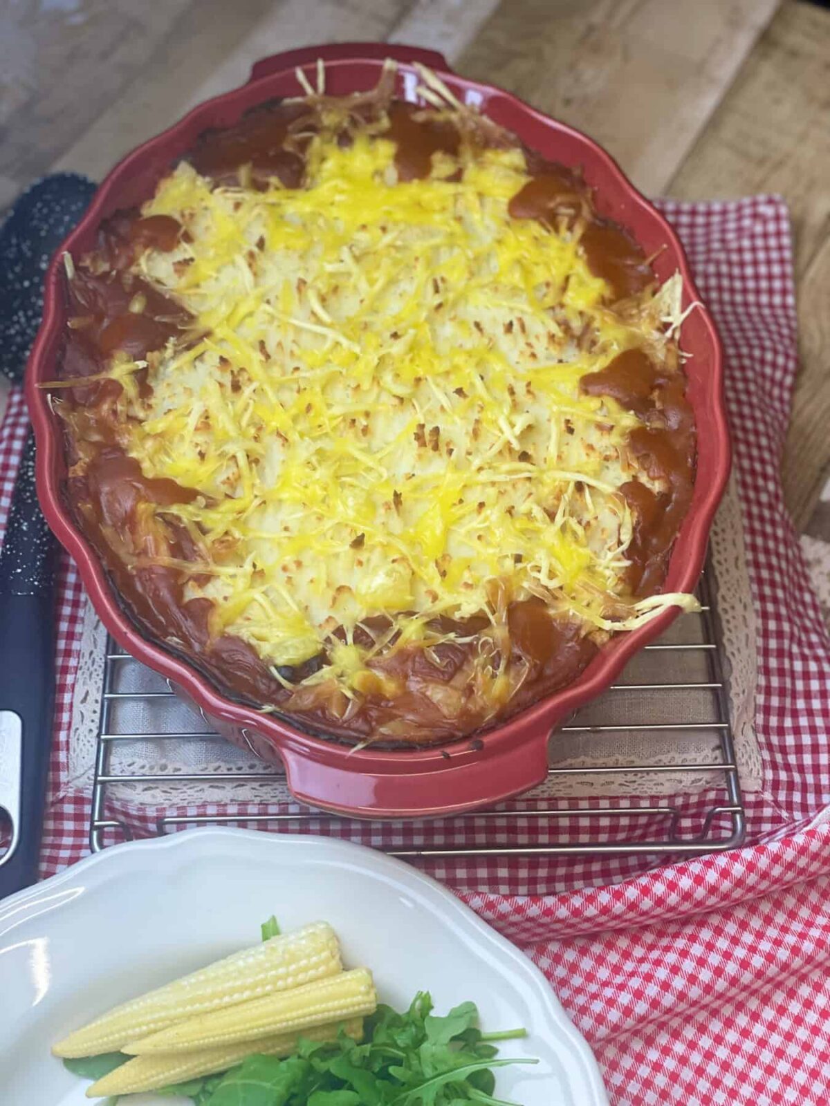 Vegan cowboy pie in red oval pie dish, black serving spoon, red check cloth.