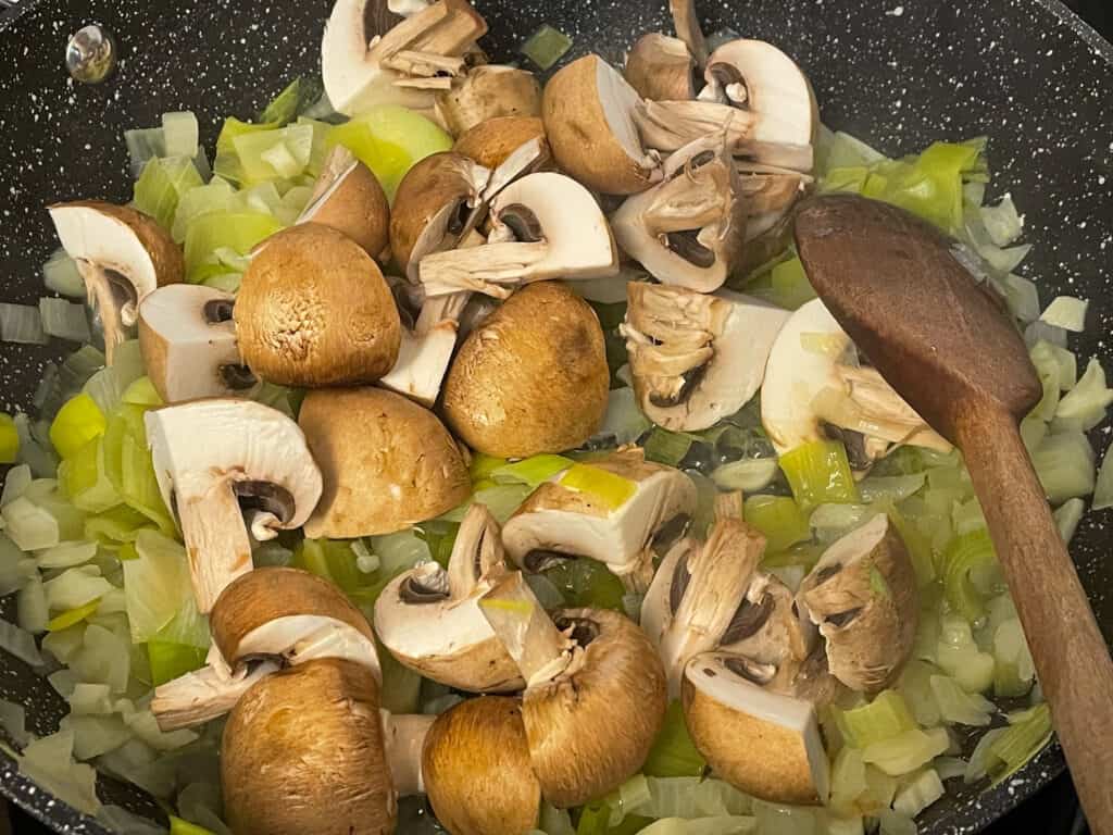 Mushrooms added to cooking pan and stirred with wooden spoon.