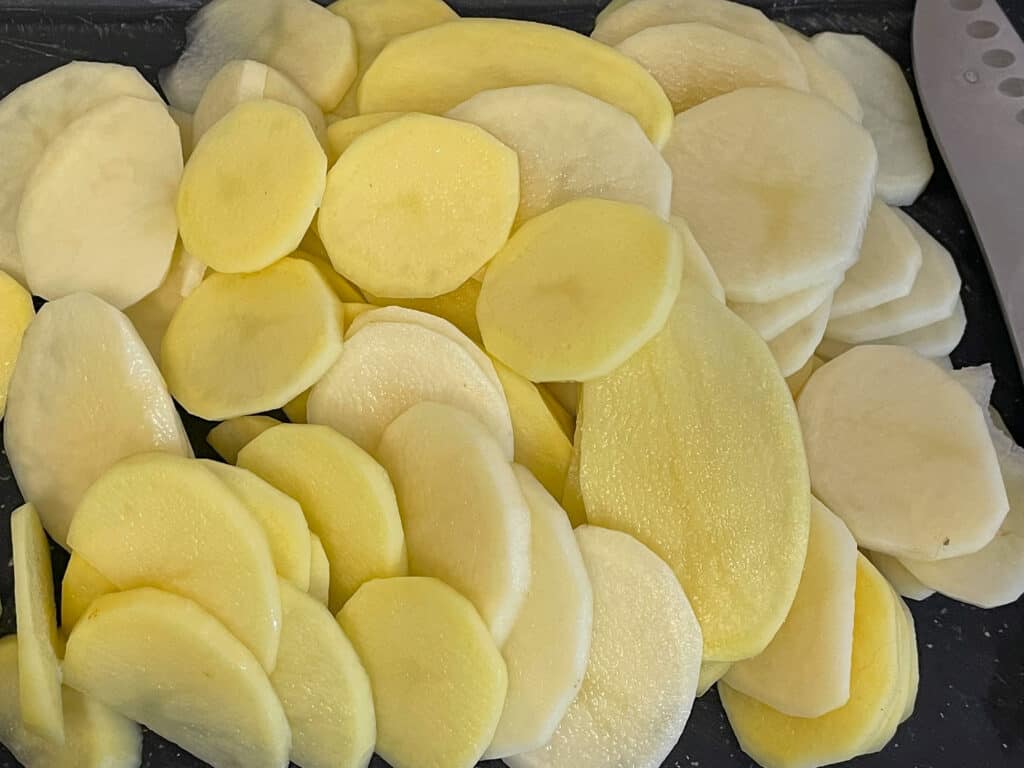 Potatoes sliced into thin discs on cutting board.