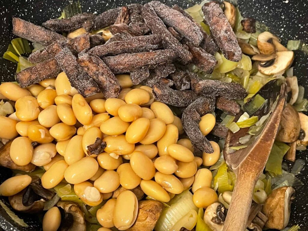 Butterbeans and meat-free beef strips added to mushrooms cooking in pan for hotpot filling.