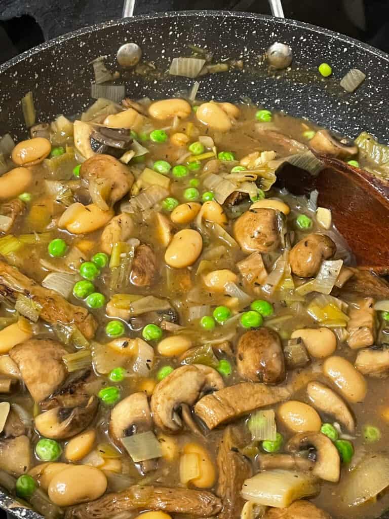 Hotpot filling cooking in skillet pan with wooden spoon stirring.