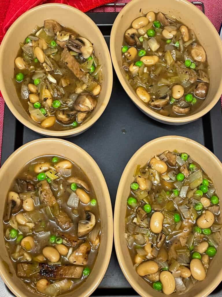 Mushroom mix divided between four individual pie dishes on baking tray.