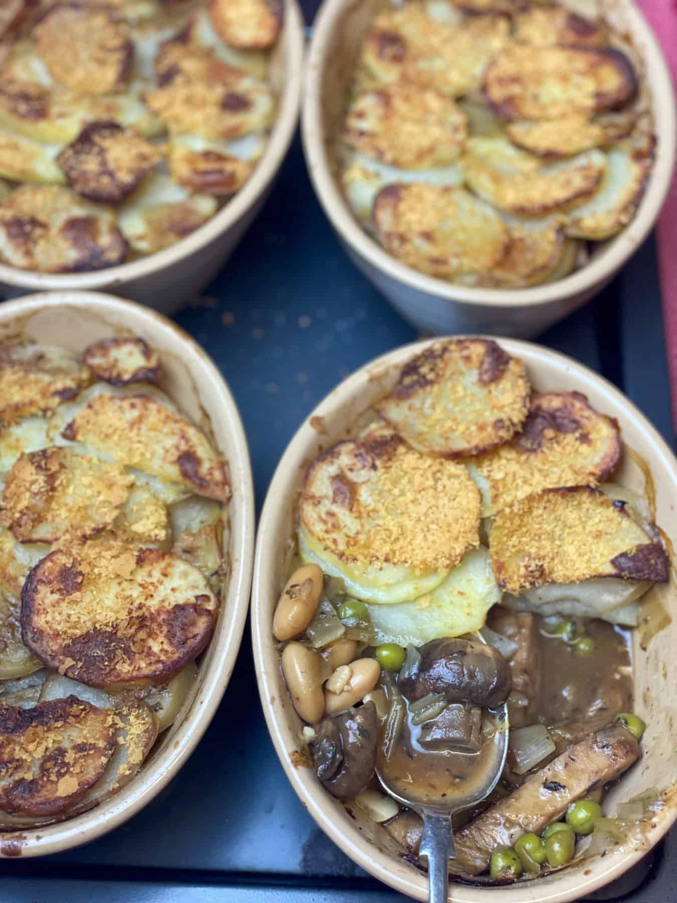 Four individual hotpots baked and golden, with part of the crispy potatoes removed to show the inside mix.