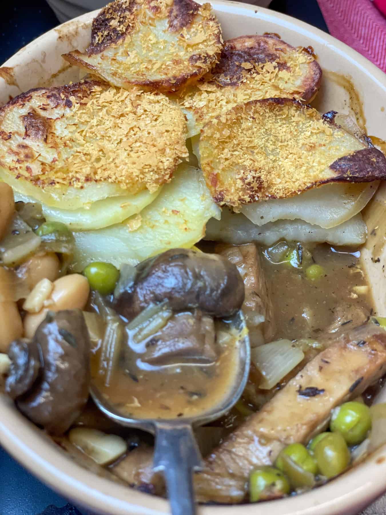 Close up of Lancashire hotpot with silver serving spoon scooping up mushroom and gravy.