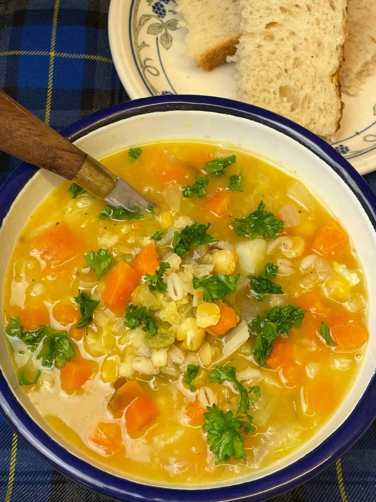 Vegan Scotch broth close up image with wooden handled spoon in bowl, bread slices to side.