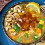 Mulligatawny soup served in blue bowl, close up with mini poppadum's, and lemon wedge.