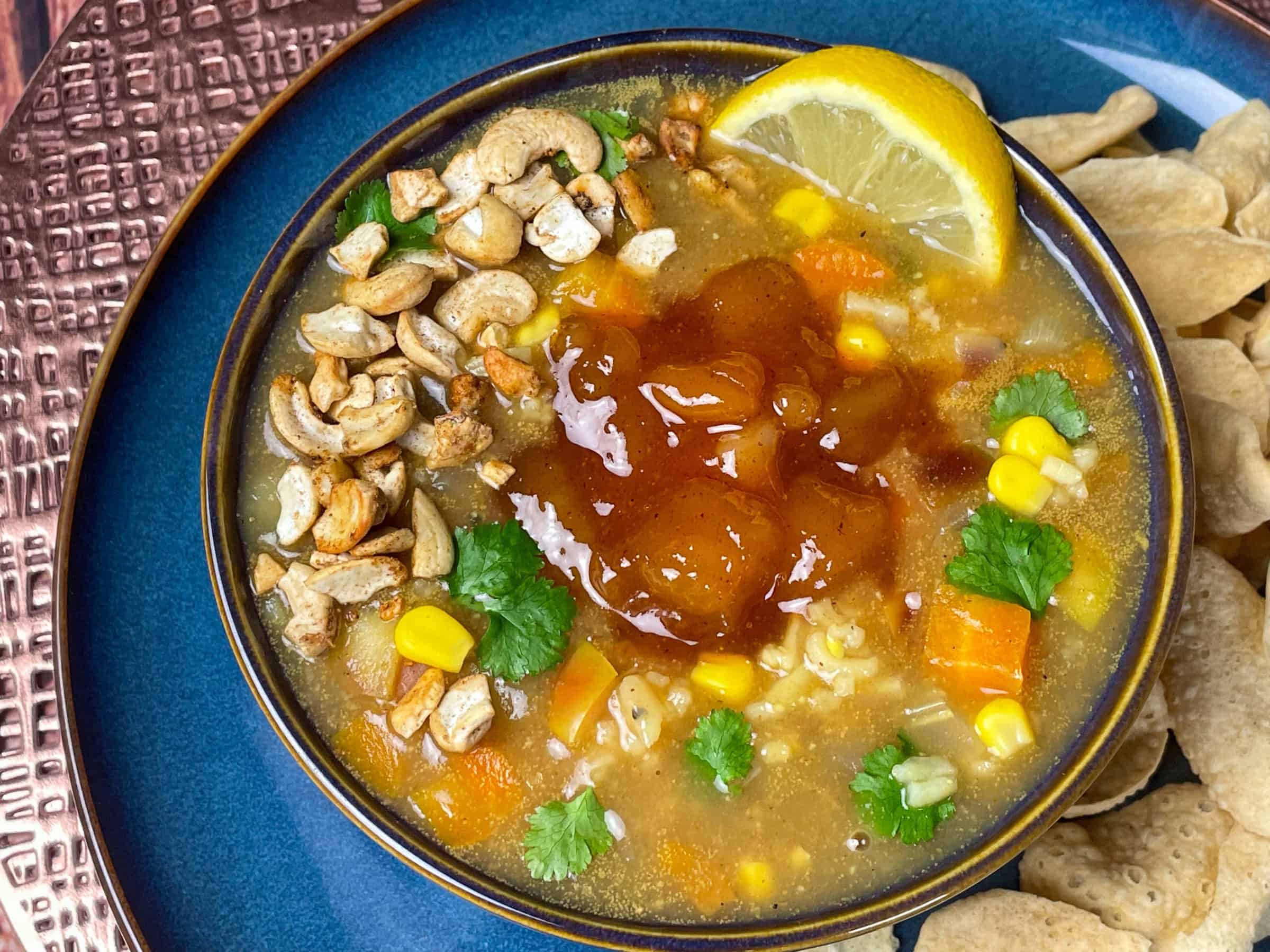 Soup served in blue bowl, close up with mini poppadum's, and lemon wedge.