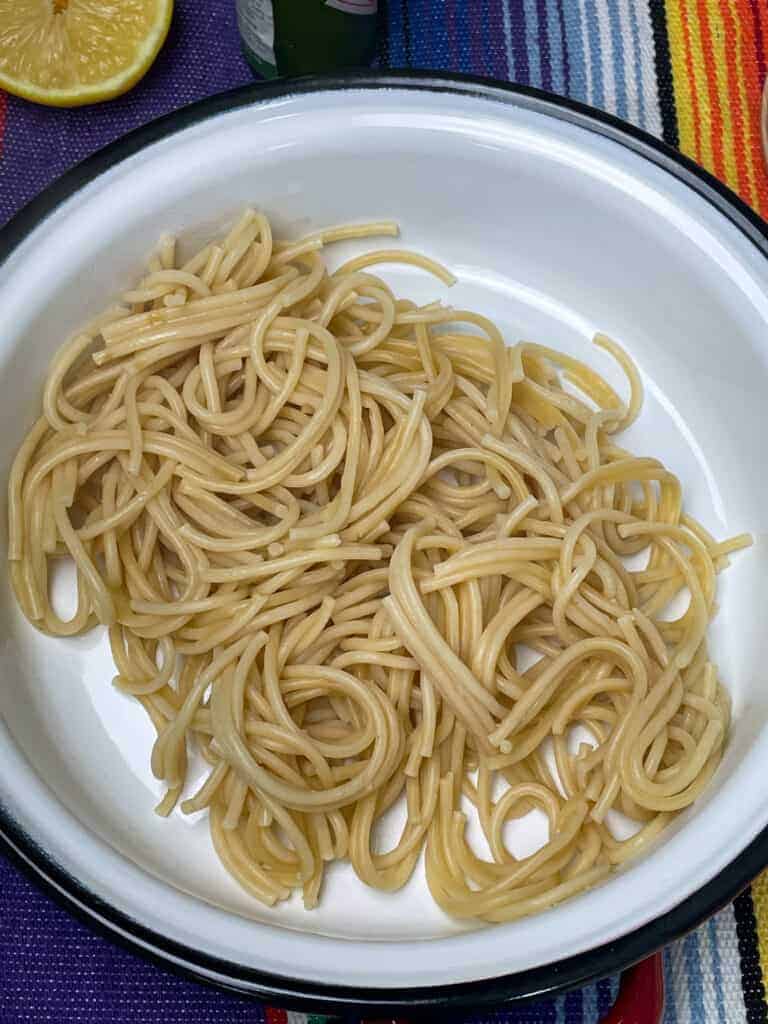 Cooked spaghetti in soup bowl, stripy colourful background.