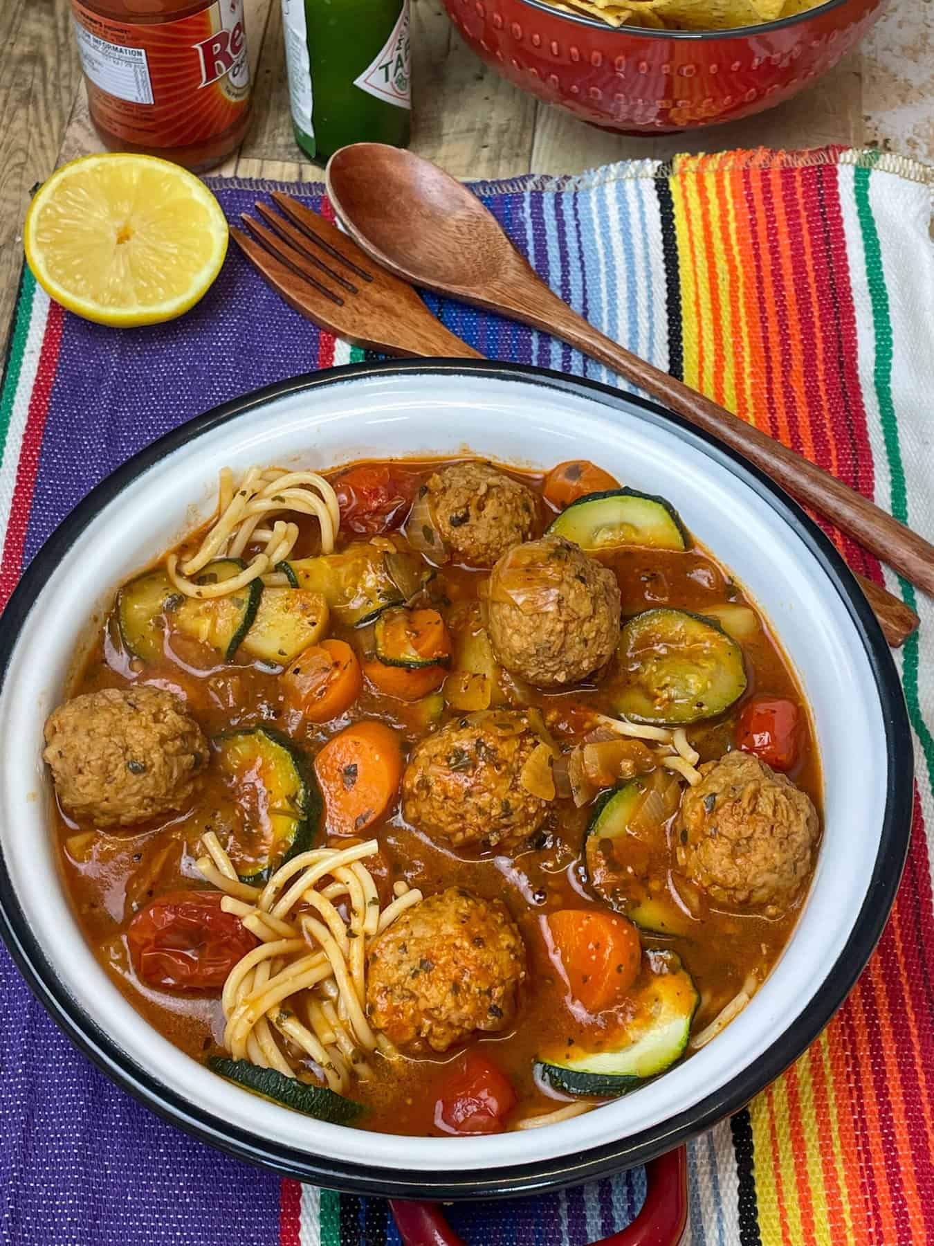 Mexican meatball soup served with hot sauce, lemon wedge, on a stripy mat.