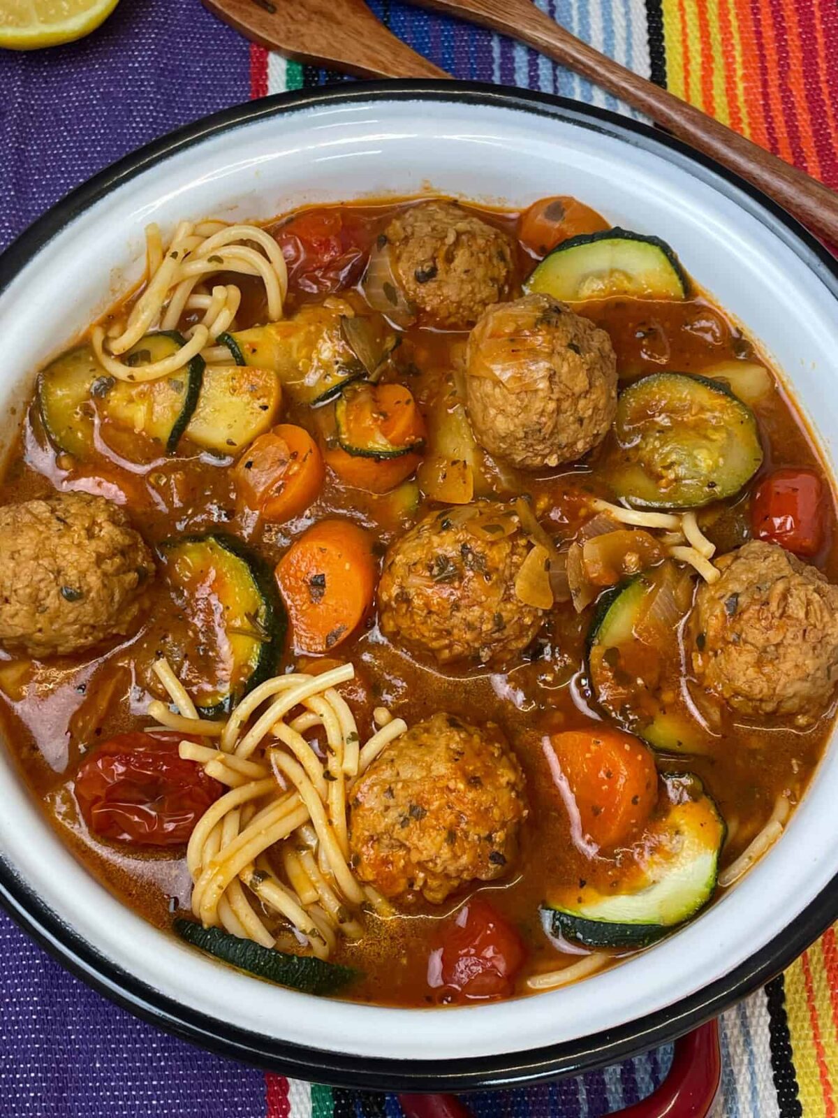 Bowl of vegan Mexican meatball soup in white bowl with dark rim, colourful background.