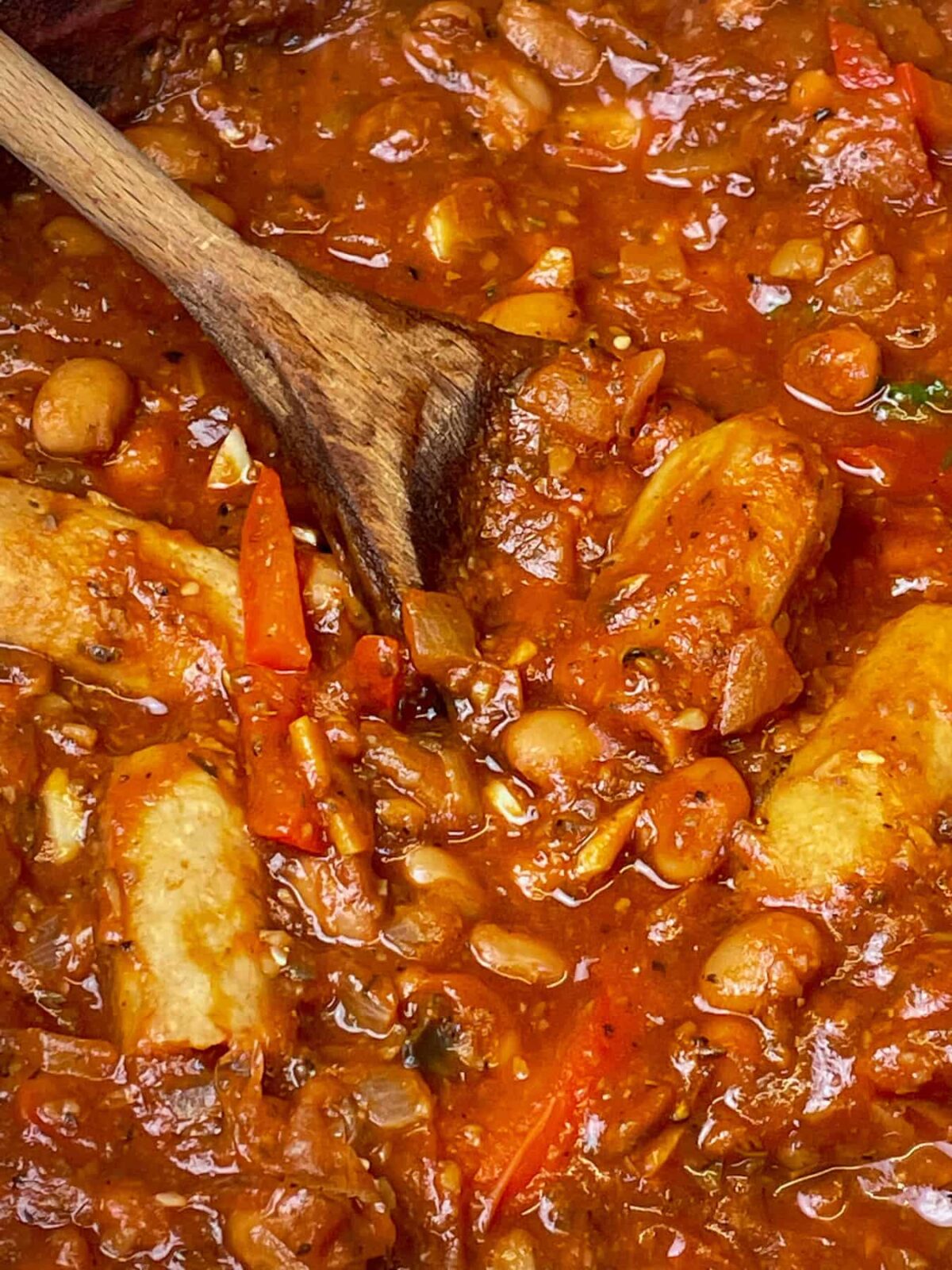 Close up of vegan sausage pasta sauce in skillet with wooden spoon.