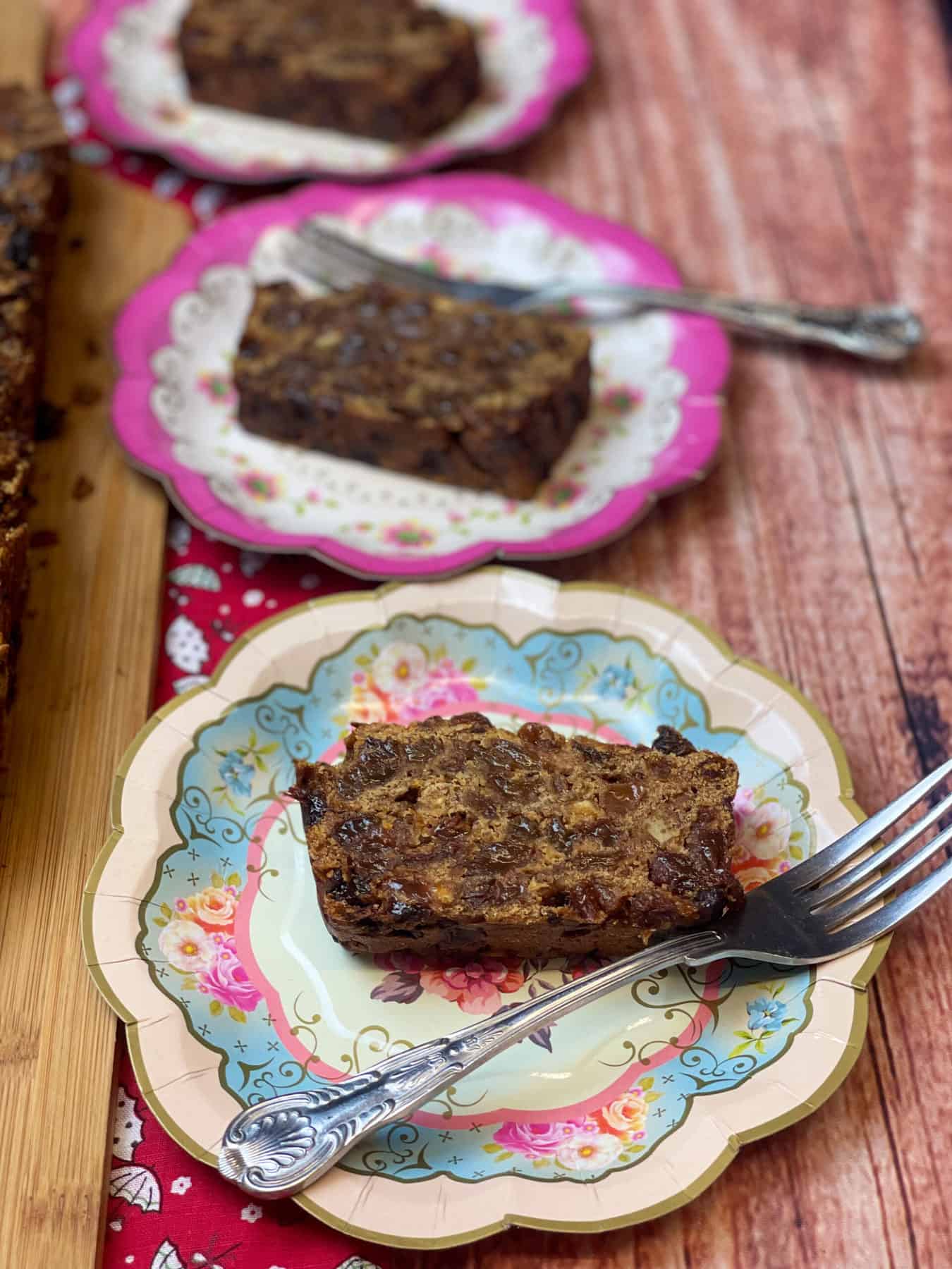 Three plates with slices of fruit cake, cake forks to side, wooden table background.