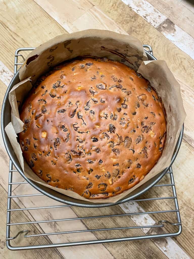 Cake baked and in cake pan on a cooling rack.