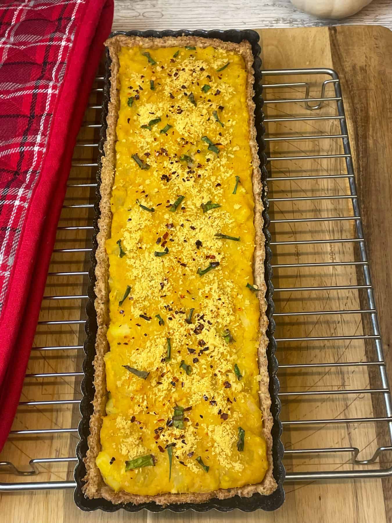 Baked harvest pumpkin and lentil pie cooling on wire rack with tartan oven mitt to side.