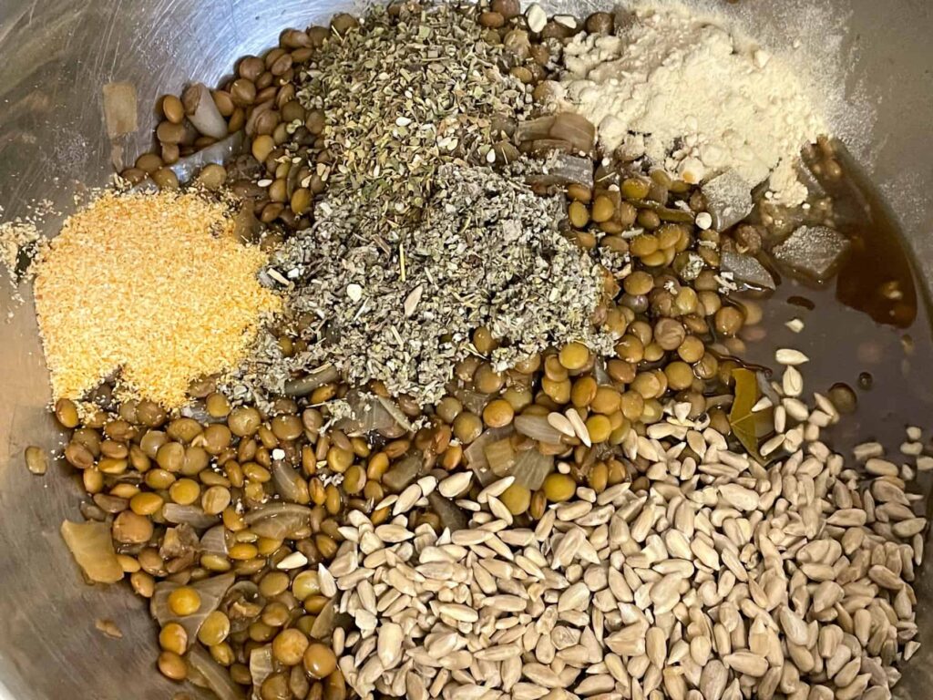 herbs and sunflower seeds added to cooked lentil mix in a mixing bowl.