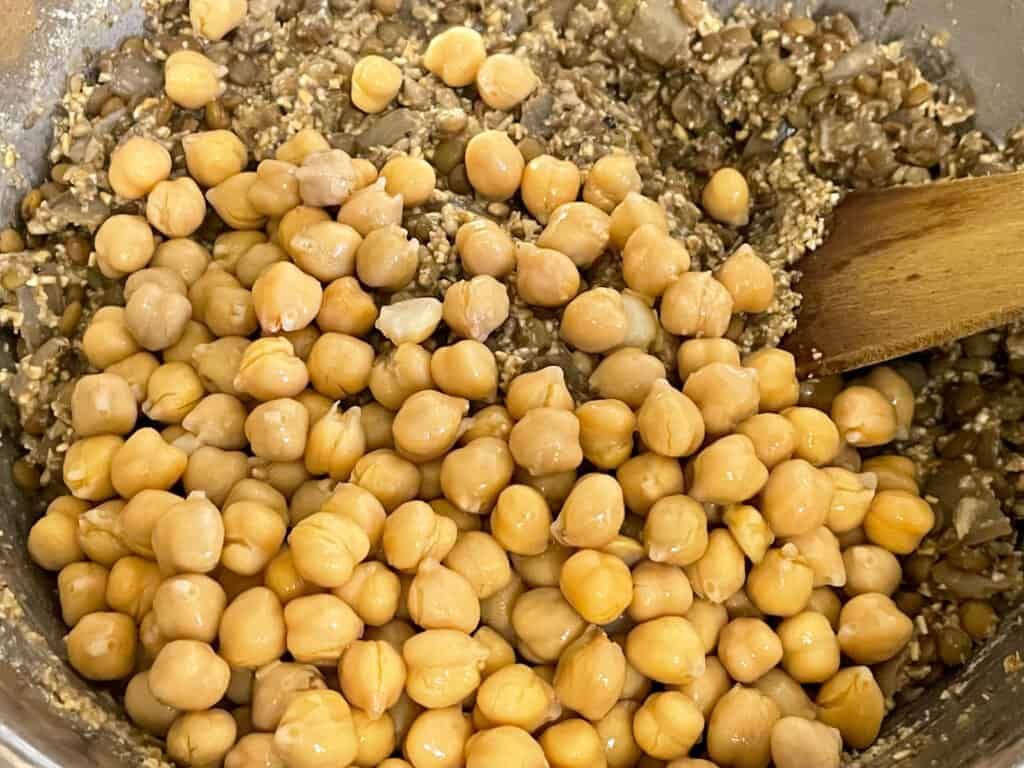 chickpeas added to lentil-oatmeal mix in bowl with spoon to side.