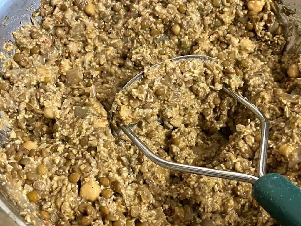 mashing up meatloaf filling with potato masher in bowl.