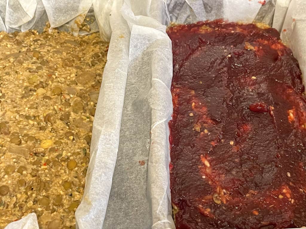 Two vegan meatloafs in loaf pans, with one spread with cranberry sauce over the top.