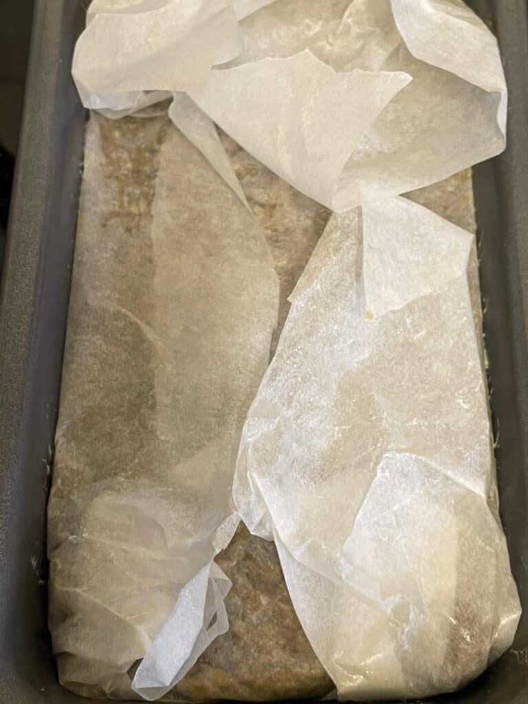 Vegan meatloaf in pan, unbaked, with greaseproof paper covering the entire meatloaf.