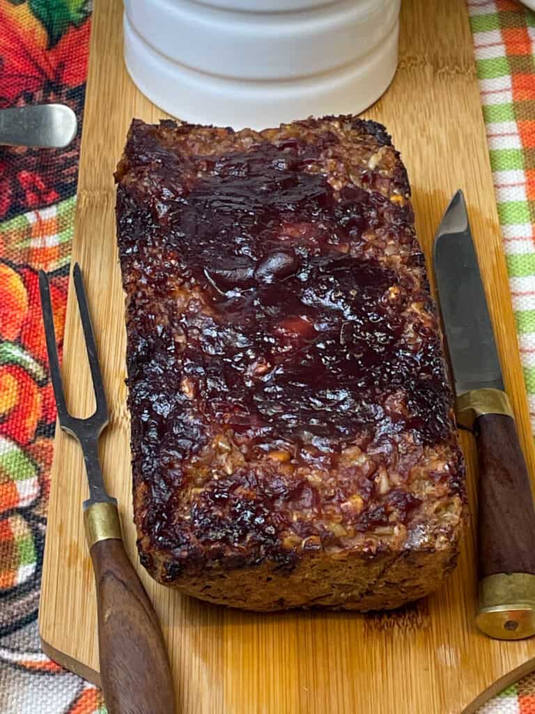 baked meatloaf with cranberry sauce served with veggie gravy in white jug, carving knife and fork to side.