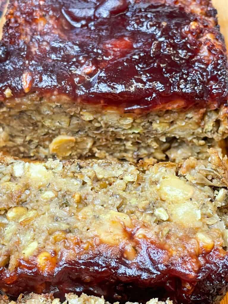 close up of vegan green lentil meatloaf with cranberry sauce spread over the top, and a slice of meatloaf cut in front.