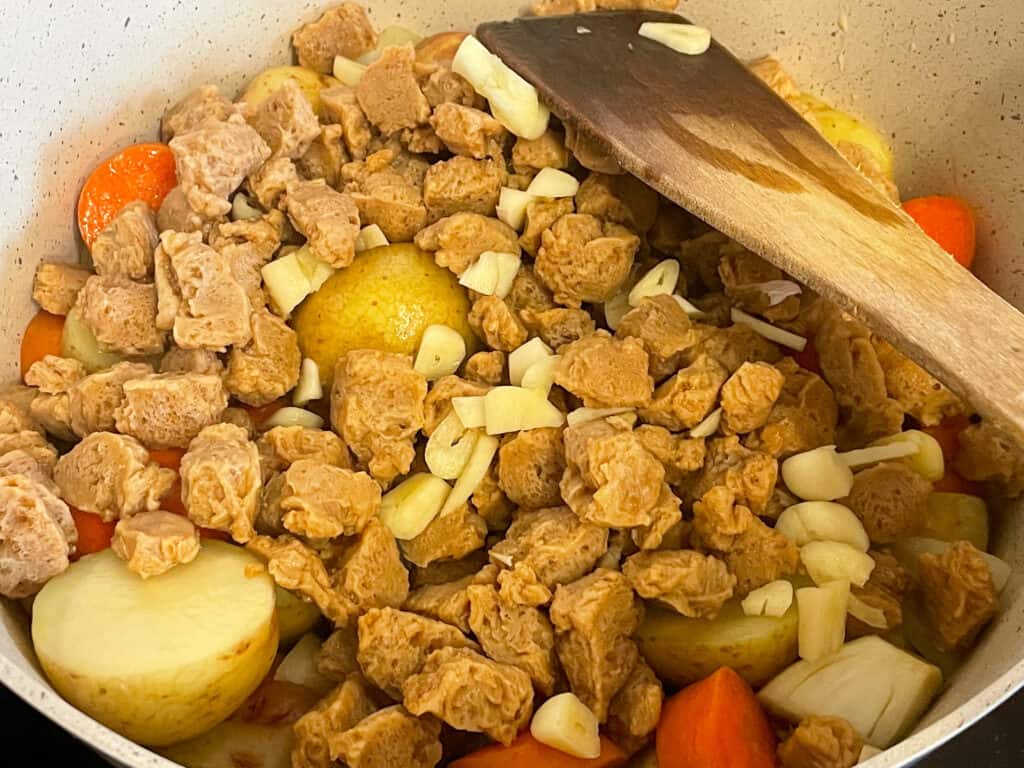 soya chunks and garlic added to chopped veggies in pan with wooden spatula.