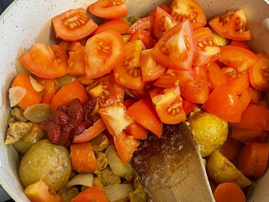 fresh chopped tomatoes added to veggies and potatoes in soup pan.
