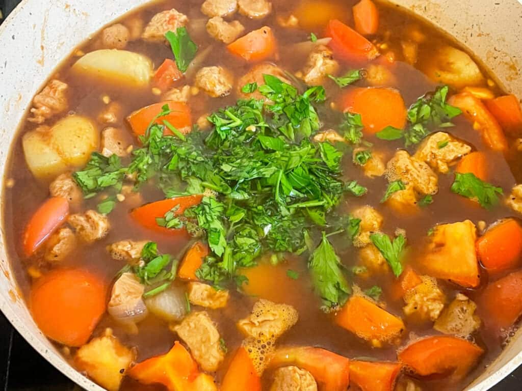 vegan stock and chopped parsley added to the beef and tomato stew in pan.