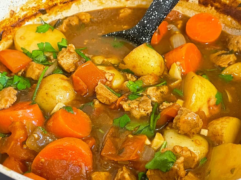 close up of vegan beef and tomato Warwickshire stew in pot with black ladle.