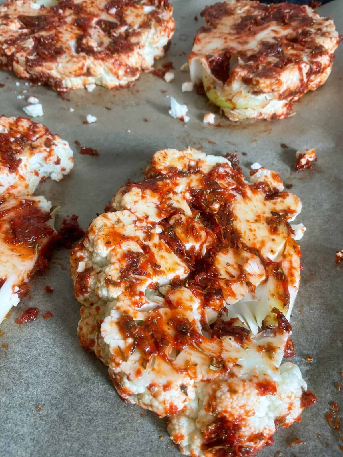 Cauliflower steaks covered in tomato paste rub and on baking tray.