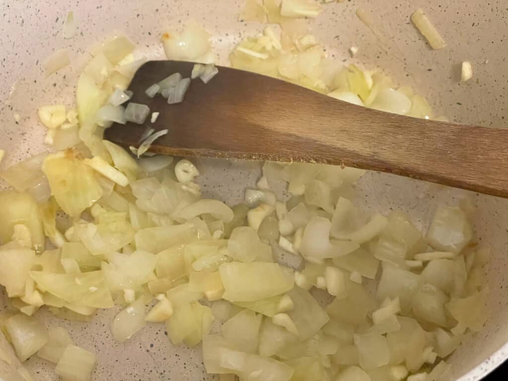 Onions and garlic cooking in white pan with wooden spatula,