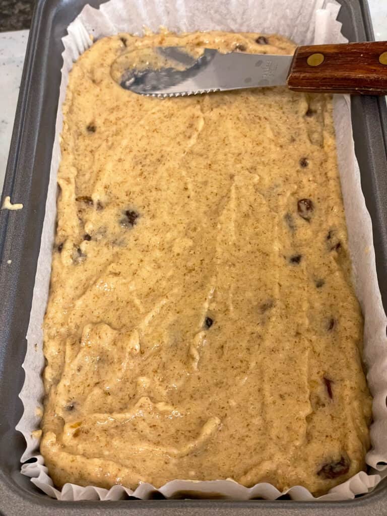 unbaked Weetabix cake added to loaf pan and a small wooden handled spatula smoothing the top down.