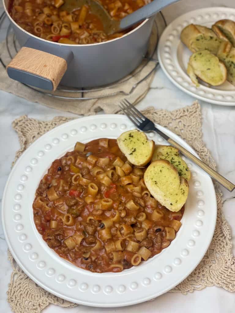 Goulash served on white bowl with pot and garlic bread in background.