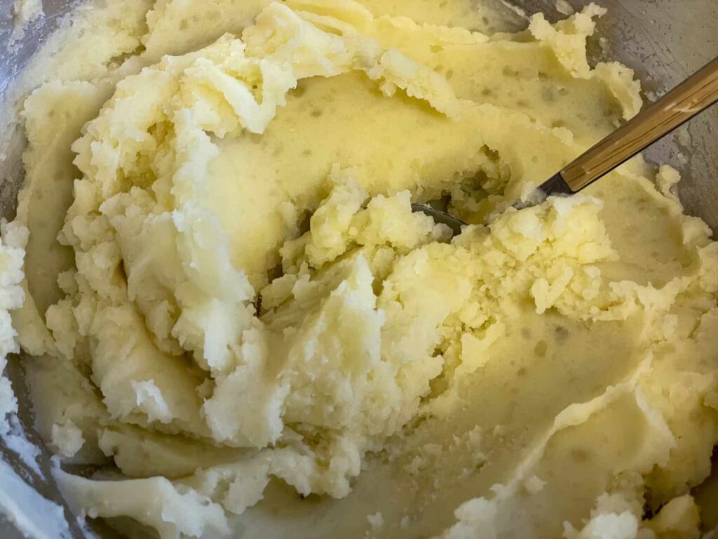 A bowl of mashed potatoes with a tan handled spoon within the potatoes.