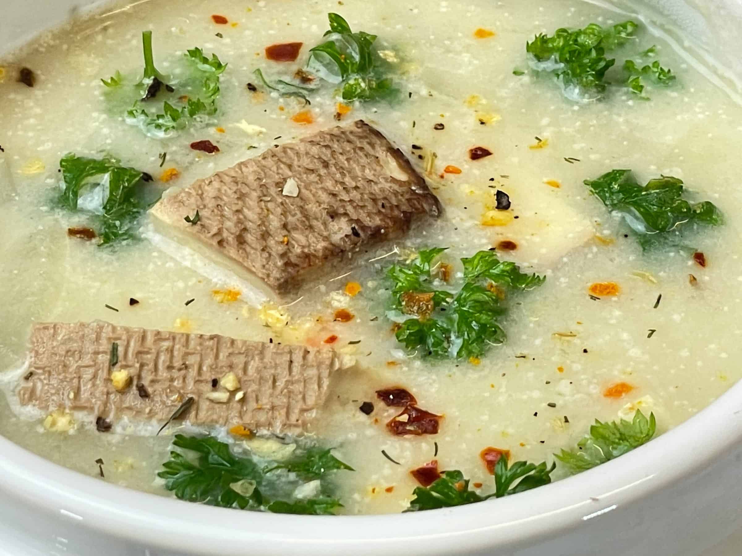 Vegan Cullen skink served in white tureen soup bowl, pieces of smoked tofu on the top along with chopped parsley and herb seasoning blend.