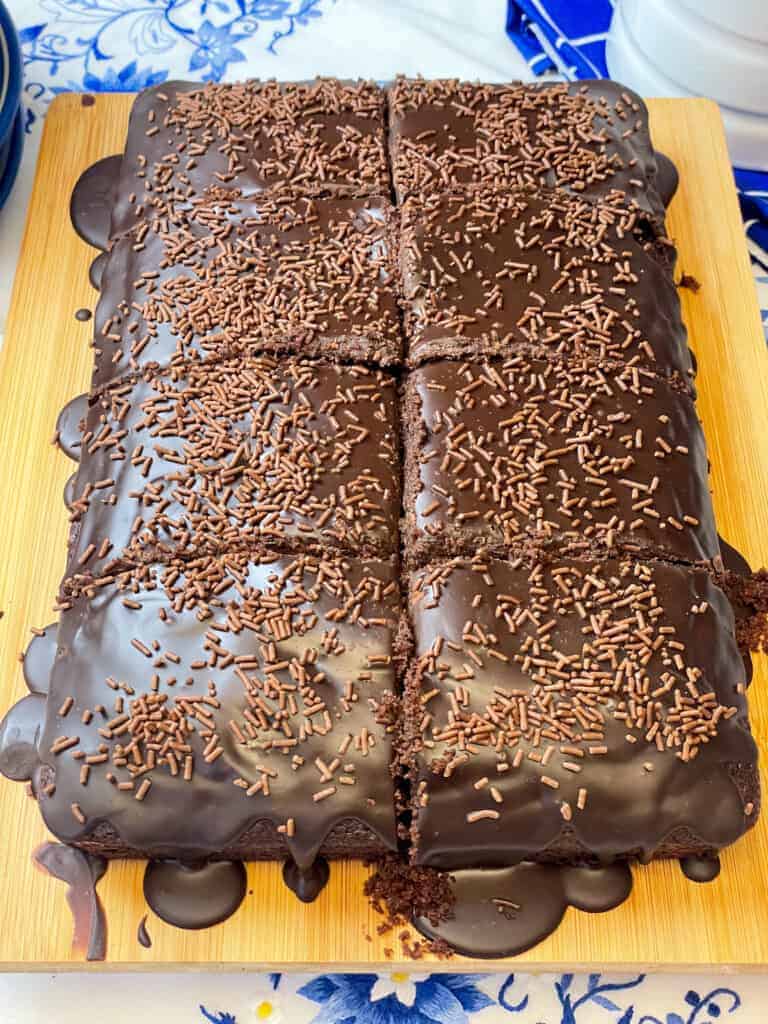 Chocolate traybake with ganache topping and sliced into 8 pieces on chopping board.