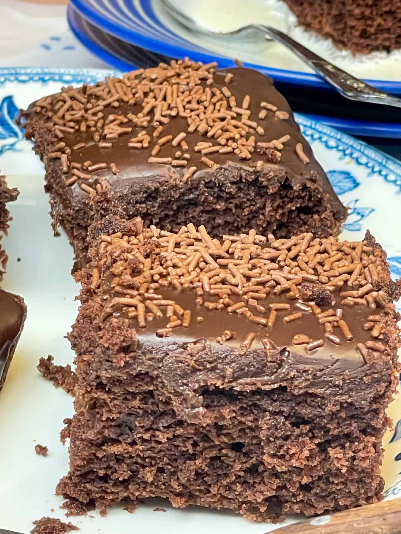 Two squares of old school dinners chocolate sponge traybake on white plate with blue flower patterns, featured image.