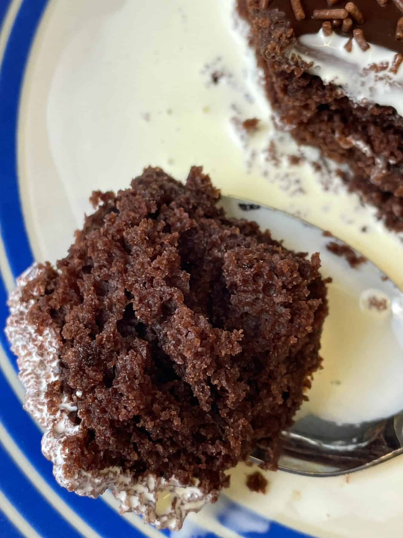 Close up of a spoonful of chocolate sponge with cream on spoon and cake plate in background.
